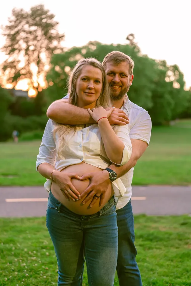 Expecting couple at golden hour, hands together in a heart over the bump